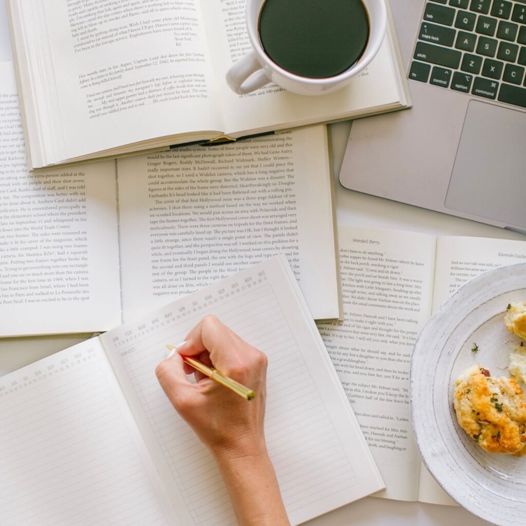 hand writing down notes next to a cup of coffee and laptop